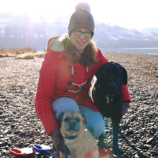 Claire Forrester photographed crouching down with her two dogs on a British stone beach.