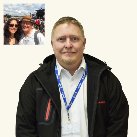 Paul Wadsley taking a selfie with his partner in front of an open air festival under the sun.